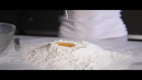 Close-Up-view-of-female-hands-breaking-the-second-egg-into-flour-on-the-kitchen-table.-Slow-Motion-shot