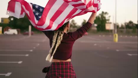 Back-view-of-a-young-happy-american-girl-running-while-holding-the-american-flag.-Then-she-turns-around-and-looks-in-the-camera