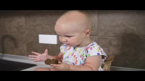 A-cute-little-baby-taking-a-piece-of-bread.-Small-cute-infant-taking-bread-and-sitting-in-the-kitchen.-Slow-Motion-shot