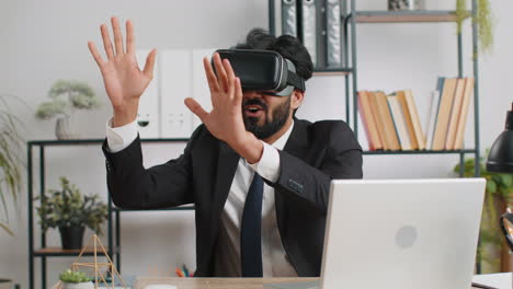 Young-business-man-in-VR-goggles-watch-virtual-reality-video,-working-on-simulation-game-at-office