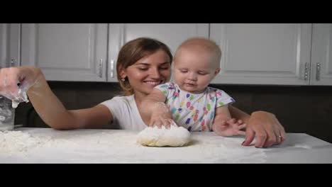 Young-mother-and-her-little-daughter-preparing-dough-on-the-table.-Baker-prepares-the-dough.-Family-girls-having-fun.-Slow-Motion