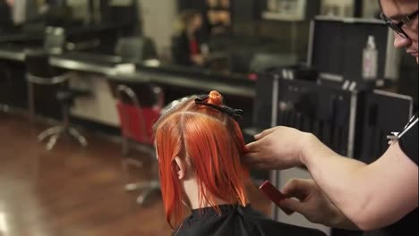 Young-woman-getting-her-hair-dressed-in-hair-salon.-Stylist-hairdresser-at-work.-Man-hairdresser-brushing-hair-in-beauty-salon