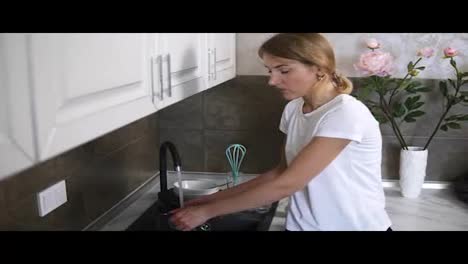 Young-blonde-woman-washing-dishes-in-a-modern-kitchen.-Slow-Motion-shot