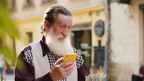 Glücklicher-älterer-Mann,-Der-Geld-Zählt,-Dollar-Bargeld,-Smartphone-Rechner-App-In-Der-Städtischen-Stadtstraße-Verwenden