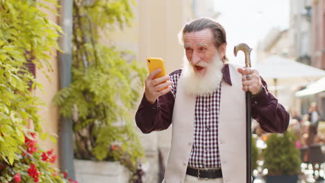 Älterer-Mann-Nutzt-Mobiles-Smartphone-Und-Feiert-Den-Gewinn-Guter-Nachrichten-Im-Freien-In-Der-Stadtstraße