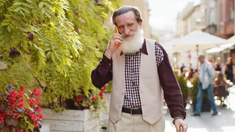 Happy-man-grandfather-having-remote-conversation-talk-on-smartphone-good-news-gossip-in-city-street