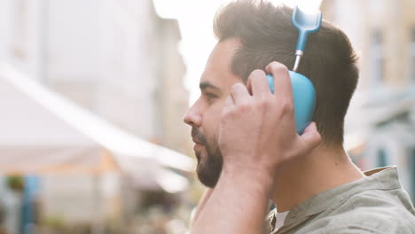 Happy-young-man-in-wireless-headphones-choosing,-listening-music-dancing-outdoors-city-street