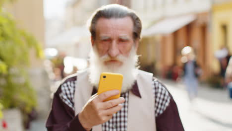 Ein-älterer-Mann-Nutzt-Sein-Smartphone,-Tippt-Textnachrichten,-Surft-Im-Internet-Und-Beendet-Seine-Arbeit-Mit-Blick-In-Die-Kamera