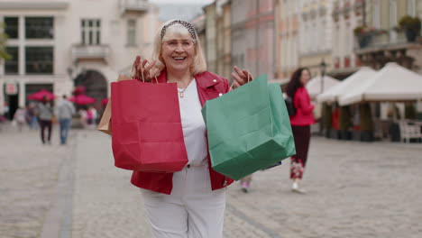 Glückliche-ältere-Frau,-Shopaholic-Verbraucherin-Nach-Dem-Einkaufsverkauf-Mit-Vollen-Taschen,-Die-In-Der-Stadtstraße-Spaziert