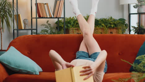 Young-woman-reading-interesting-book-turning-pages-smiling-enjoying-literature-taking-rest-on-sofa