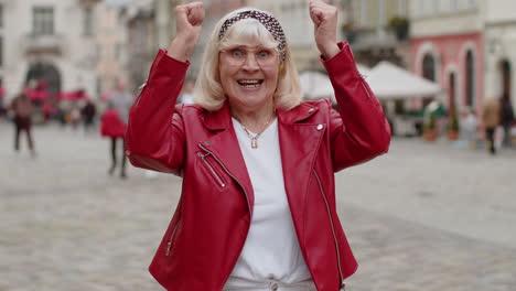Senior-woman-shouting,-celebrating-success-winning-goal-achievement-good-victory-news-in-city-street