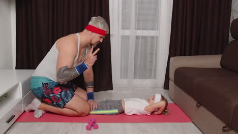 Sportsman-trainer-man-working-out-with-child-kid-girl,-abs-exercises-with-daughter-at-home-on-mat