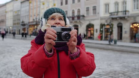 Senior-old-woman-tourist-taking-pictures-with-photo-camera,-using-retro-device-in-winter-city-center