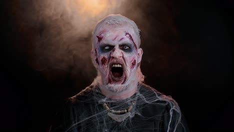 Sinister-man-in-costume-of-Halloween-crazy-zombie-with-bloody-wounded-scars-face-screaming,-shouting