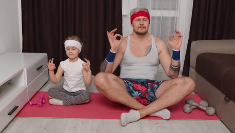 Retro-style-father-and-cute-little-kid-daughter-meditating-in-lotus-pose-at-home,-yoga-exercises