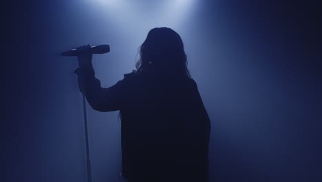 Backlit-silhouette-of-singer-vocalist-girl-standing-in-dark-nightclub-disco-studio-and-start-singing