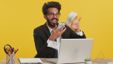 Cheerful-rich-business-man-working-on-office-laptop-wasting-throwing-money-to-camera-profit-win