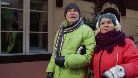 Happy-senior-couple-tourists-man-and-woman-walking,-talking,-gesturing-in-winter-snowy-European-city