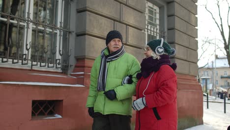 Senior-couple-man,-woman-tourists-walking-in-old-city-in-winter-talking,-gesturing-holidays-vacation