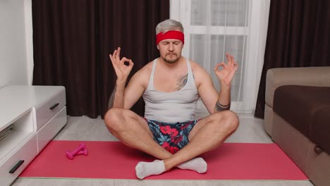 Retro-male-model-guy-calms-down,-practicing-yoga-meditating-at-home-sitting-in-relaxing-lotus-pose