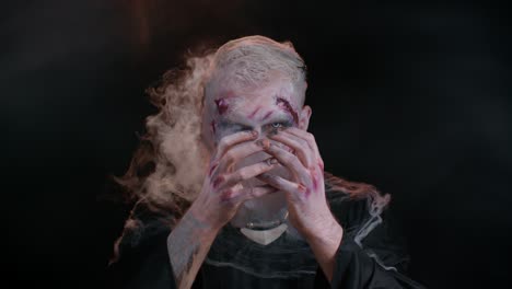 Sinister-man-with-horrible-scary-Halloween-zombie-makeup-in-costume-blows-smoke-from-nose-and-mouth
