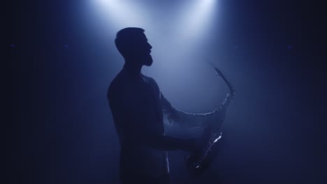Backlit-silhouette-of-saxophonist-man-with-saxophone-in-dark-nightclub-studio-and-start-playing-sax
