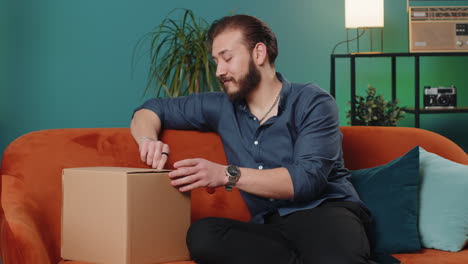 Happy-lebanese-man-shopper-unpacking-cardboard-box-delivery-parcel-online-shopping-purchase-at-home
