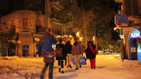 People-walk-through-unusually-snowy-streets-past-Noya-restaurant-in-Jerusalem-at-night