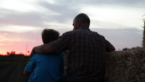 A-father-and-son-sit-in-a-farm-field-at-sunset-2