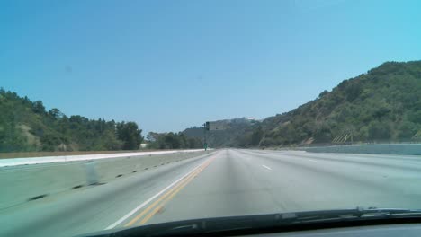 Car-driving-down-an-empty-stretch-of-freeway-in-Los-Angeles-with-construction-vehicles-visible-in-the-closed-down-lanes-at-left
