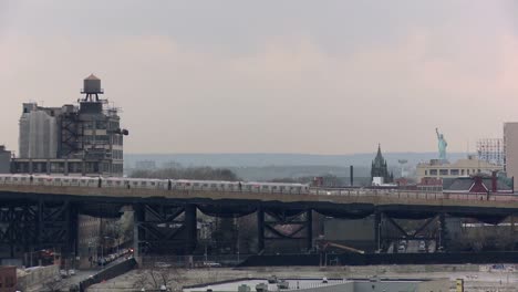 An-elevated-train-passes-by-with-the-Statue-of-Liberty-visible-in-the-background