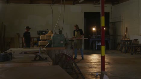 A-woodworker-places-a-plank-on-a-workbench-while-a-forklift-maneuvers-in-the-background