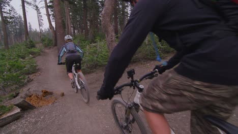 POV-shot-of-mountain-bikers-riding-on-a-dirt-path-through-a-forest