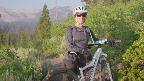 A-mountain-biker-stands-with-her-bike-on-a-path-near-a-forest