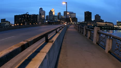 Peatones-Y-Vehículos-Cruzan-Un-Puente-En-El-Centro-De-Minneapolis-Mientras-El-Cielo-Se-Oscurece-Hasta-Convertirse-En-Noche