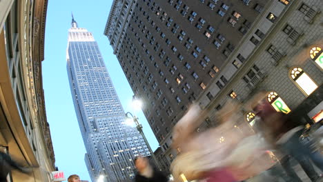 The-Empire-State-Building-is-framed-by-blue-sky-as-accelerated-traffic-and-pedestrians-pass-in-the-foreground