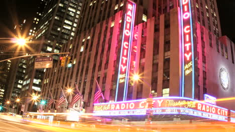 Slow-downward-pan-of-an-accelerated-shot-of-traffic-passing-in-front-of-Radio-City-Music-Hall-at-night