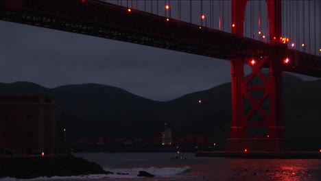 Kleine-Boote,-Die-Nachts-Unter-Der-Golden-Gate-Bridge-Hindurchfahren,-Werden-Von-Der-Riesigen-Struktur-In-Den-Schatten-Gestellt
