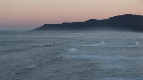 Mist-Lies-Above-The-Ocean-Waves-Rolling-Towards-Shore-Beneath-A-Pastel-Sky