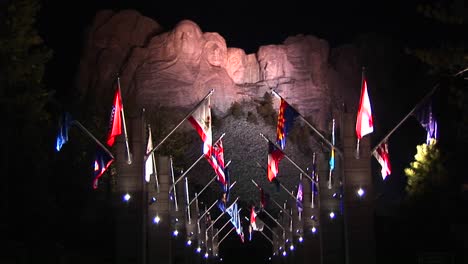 Ein-Nächtliches-Blick-Auf-Den-Mt-Rushmore-In-Lichtern-Mit-Der-Allee-Der-Flaggen-Im-Vordergrund