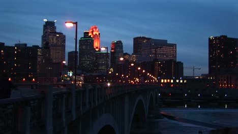 Medium-Wide-Shot-Of-Night-Traffic-On-Bridge-Over-The-Mississippi-River-Along-The-Waterfront-Of-Minneapolis-Minnesota