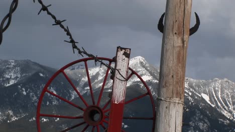 Medium-Shot-Of-Western-Mountains-Red-Wagonwheel-Rim-Barbedwire-And-Cattle-Horns-Tacked-To-A-Pole