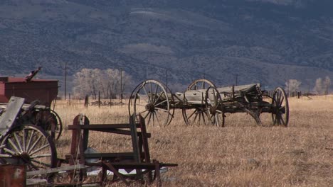 A-Scenic-Look-At-Old-Wagons-And-Other-Vintage-Equipment-Abandoned-On-The-Prairie-With-The-Mountains-Rising-In-The-Background