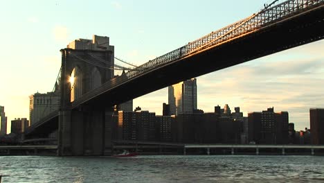 Die-Kamera-Schießt-Vom-Wasserspiegel-Auf-Die-Brooklyn-Bridge-Oben-Und-Gebäude-Dahinter