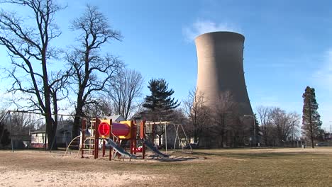Un-Colorido-Parque-Infantil-Se-Ve-En-Primer-Plano-Con-Una-Planta-De-Energía-Nuclear-En-El-Fondo