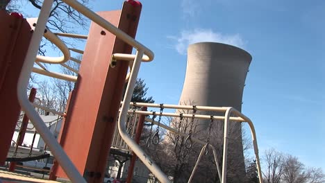 Children'S-Playground-Equipment-Is-Being-Used-While-A-Nuclearpower-Plant-Is-Shown-In-The-Background