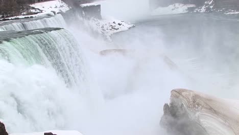 The-Camera-Looks-Down-On-Niagara-Falls-With-A-Large-Ice-Chunk-In-The-Foreground