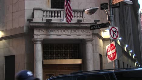 The-Camera-Pans-Up-From-The-Bronze-Door-Entrance-Of-The-New-York-Stock-Exchange-To-The-American-Flag-And-The-Wall-Street-Sign