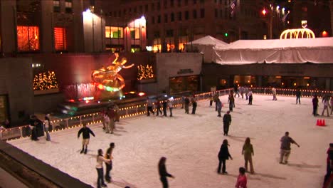 The-Camera-Shows-Skaters-At-Night-On-The-Rockefeller-Center-Ice-Rink-And-Then-Pans-Up-The-Ge-Building