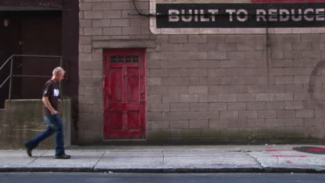 A-Young-Man-Walks-By-Old-Building-With-A-Red-Door